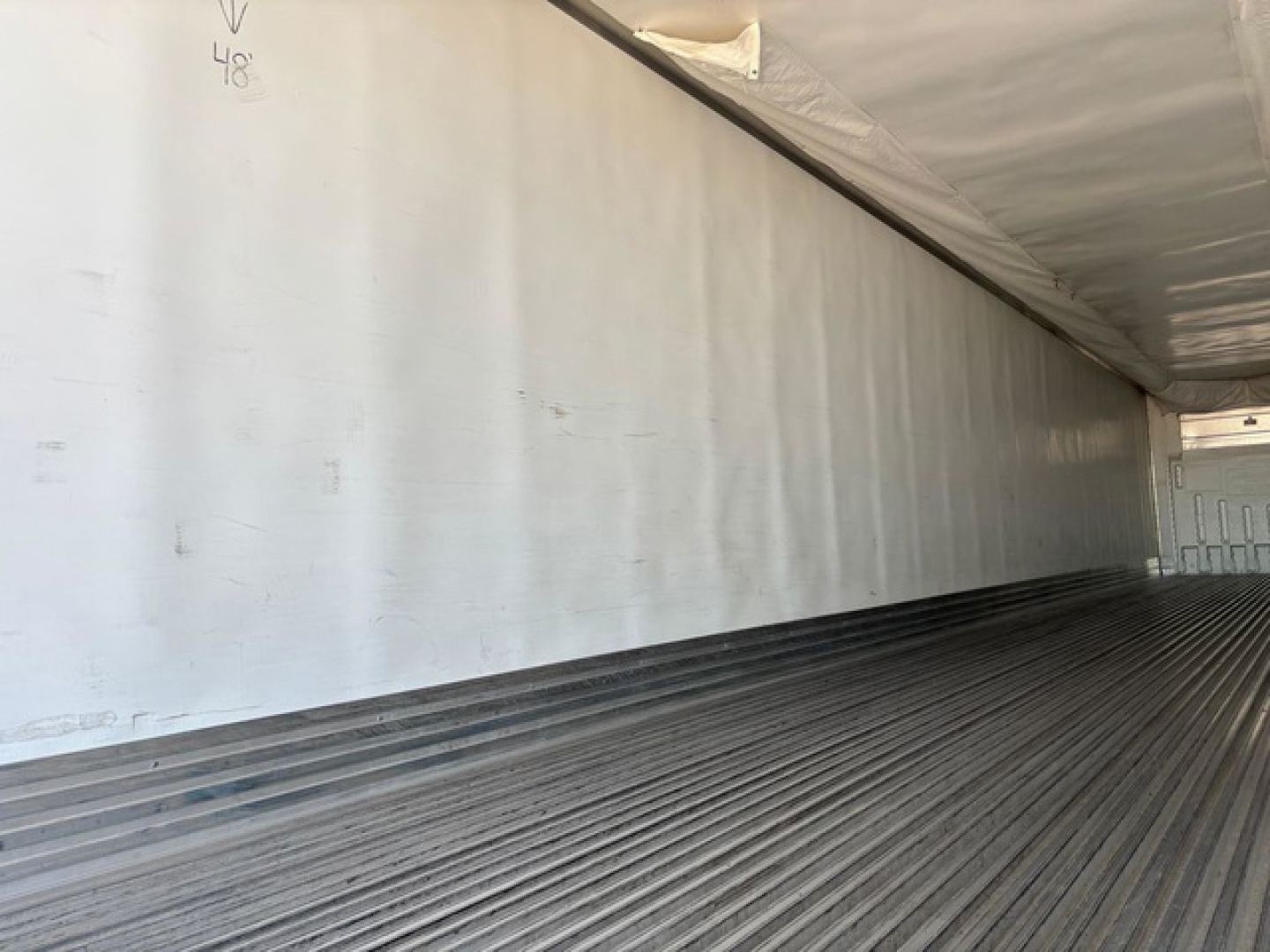 Truck trailer interior with ribbed floor and side wall; faint markings '48' and a small arrow on wall.