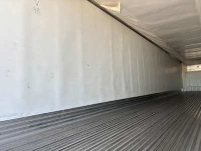 Truck trailer interior with ribbed floor and side wall; faint markings '48' and a small arrow on wall.