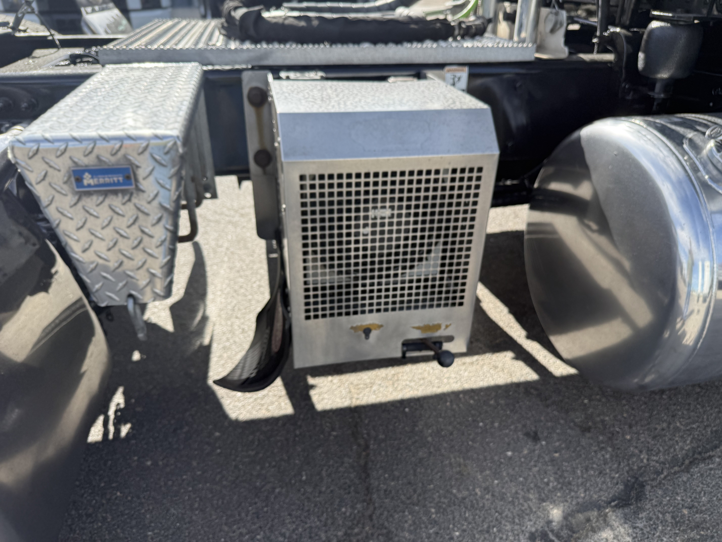 Peterbilt 389 truck undercarriage showing auxiliary air filter housing and metal toolbox with diamond plate pattern.
