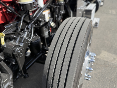 Front wheel and engine bay of a Peterbilt 389 showing a dual-rail tire and suspension components.