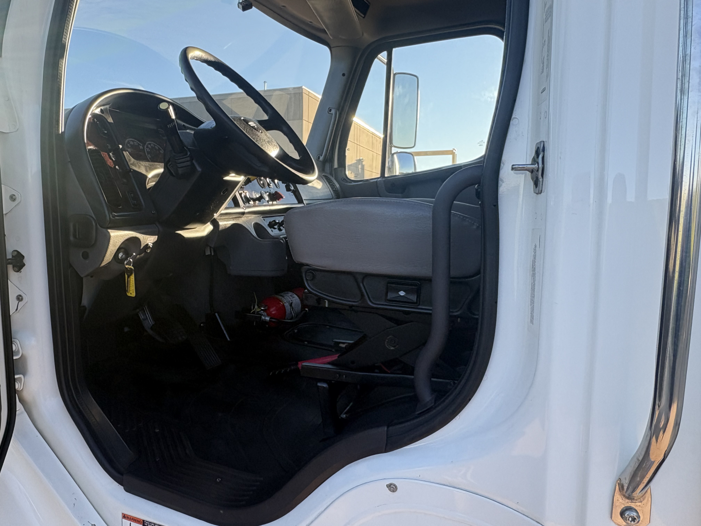 Cab interior of a 2022 Freightliner M2-106 truck showing steering wheel, driver seat, and dashboard with a fire extinguisher mounted under the dash.