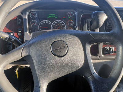 Dashboard and steering wheel of a Freightliner M2-106 showing instrument cluster with gauges and center digital display, steering wheel badge reading Freightliner.