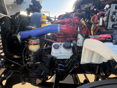 Freightliner M2-106 engine bay showing red turbo/intercooler piping, blue hose, white reservoir, and various wiring in view.