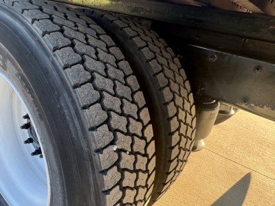 Truck rear wheel and chassis of a Freightliner M2-106 showing dual tires with tread pattern; part of the frame and a suspension component visible.