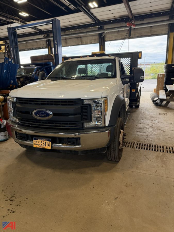 Ford F-550 truck in a shop bay showing front grille and headlights with NY plate and crane equipment in background.