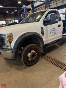 Ford F-550 crane truck front-left view showing wheel, cab with Oswego logo, and service bay interior.
