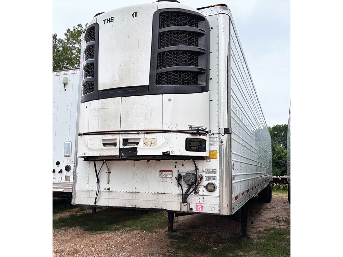 Trailer front view of a white 2018 Utility 3000R refrigerated trailer with black cooling unit panels and service area, showing front base and landing legs.