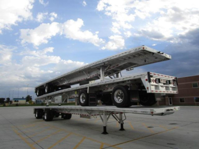Flatbed trailer with extended lift showing aluminum frame and tandem axles, new condition, flatbed raised in a lot.