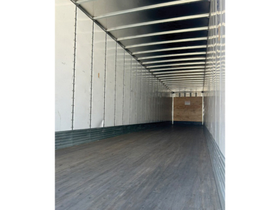 Trailer interior showing empty cargo space with metal walls and wooden bulkhead at far end.