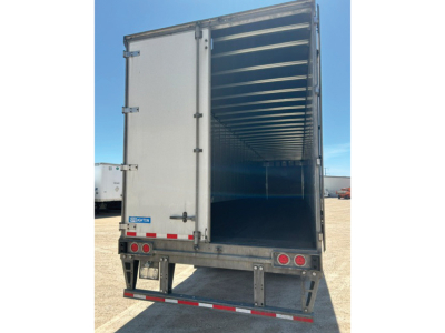 Trailer interior view from rear with open doors showing empty cargo area and metal ribbed walls.
