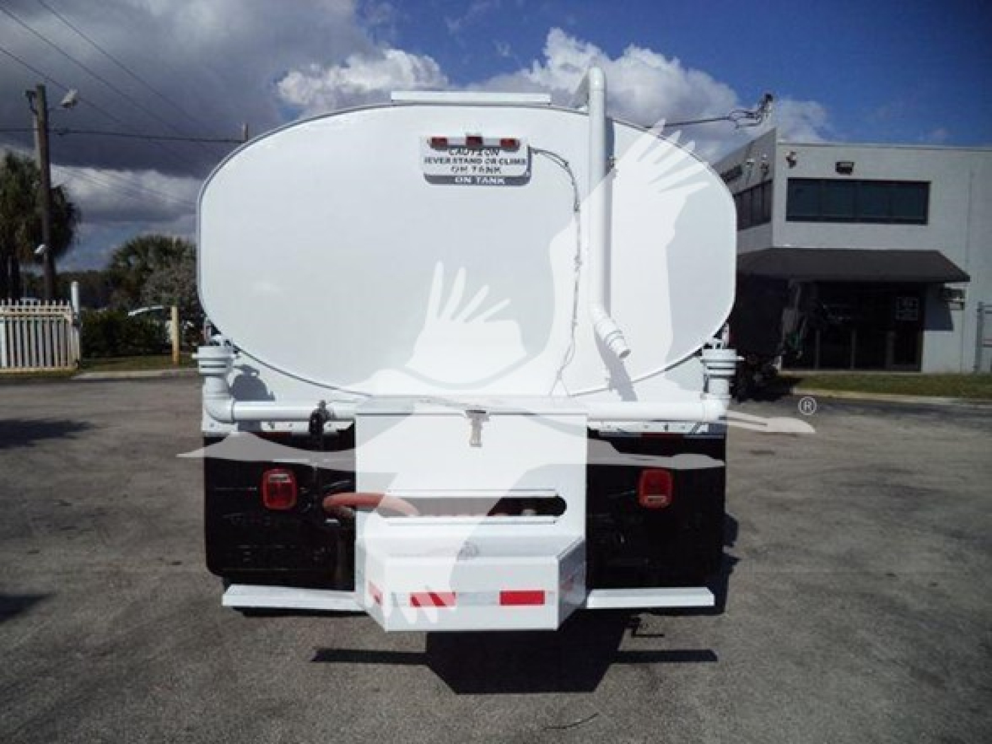 Rear view of a white Hino 338 tank truck showing rear bumper, lights, and a tanker hatch with a small label; no legible serials visible.