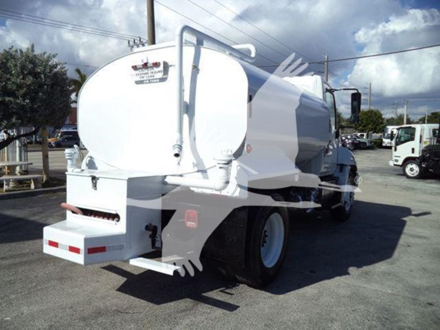 Large white tanker truck rear and side view with rounded tank, rear platform and bumper. Visible labels/decals include a small sticker on the back around the top, and a red/white reflective bumper.