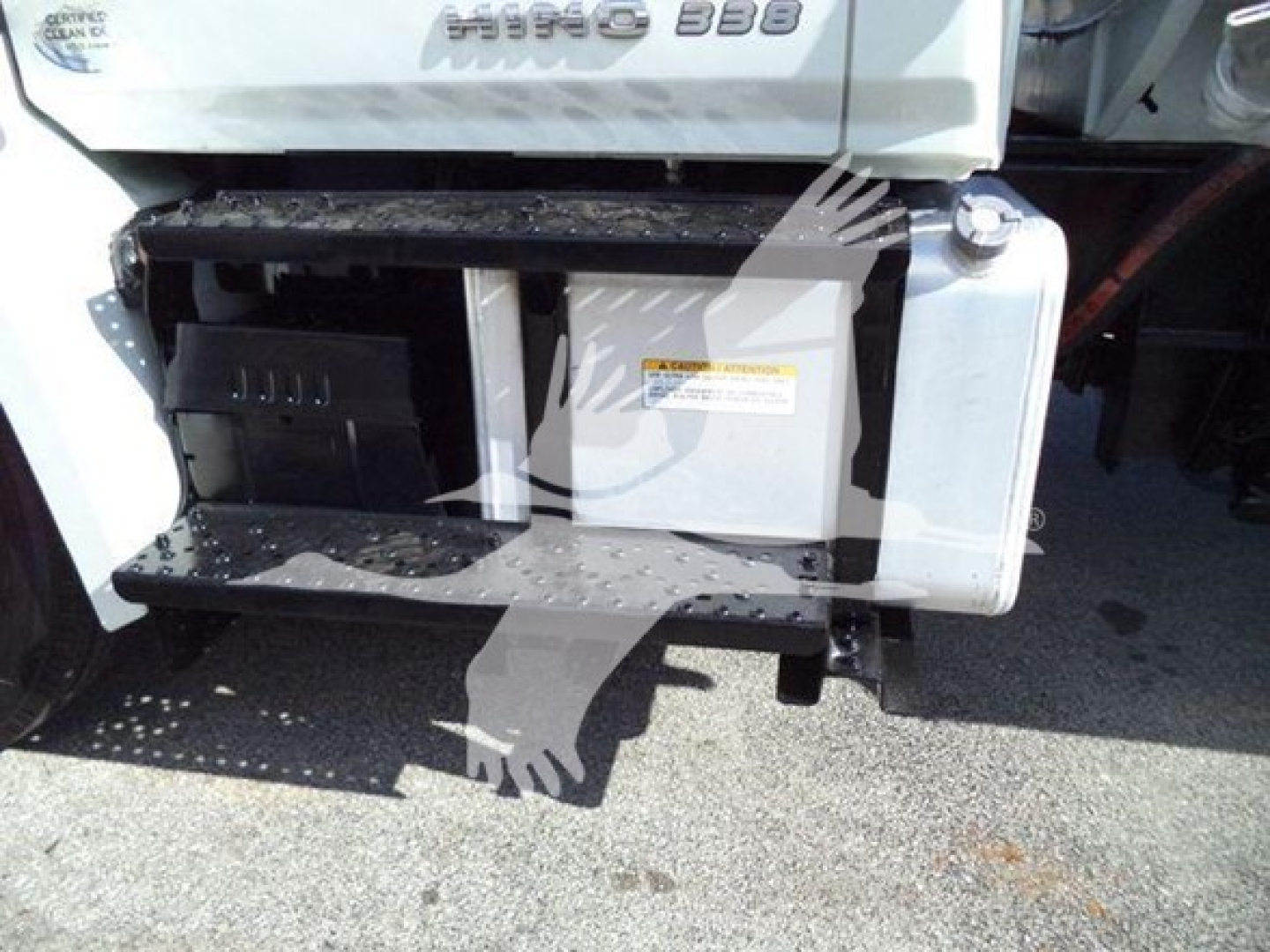 Truck side view showing steps and fuel tank with warning label and compartment doors. Partial badge reads 'HINO 338' on cab along with a warning label on the side panel.