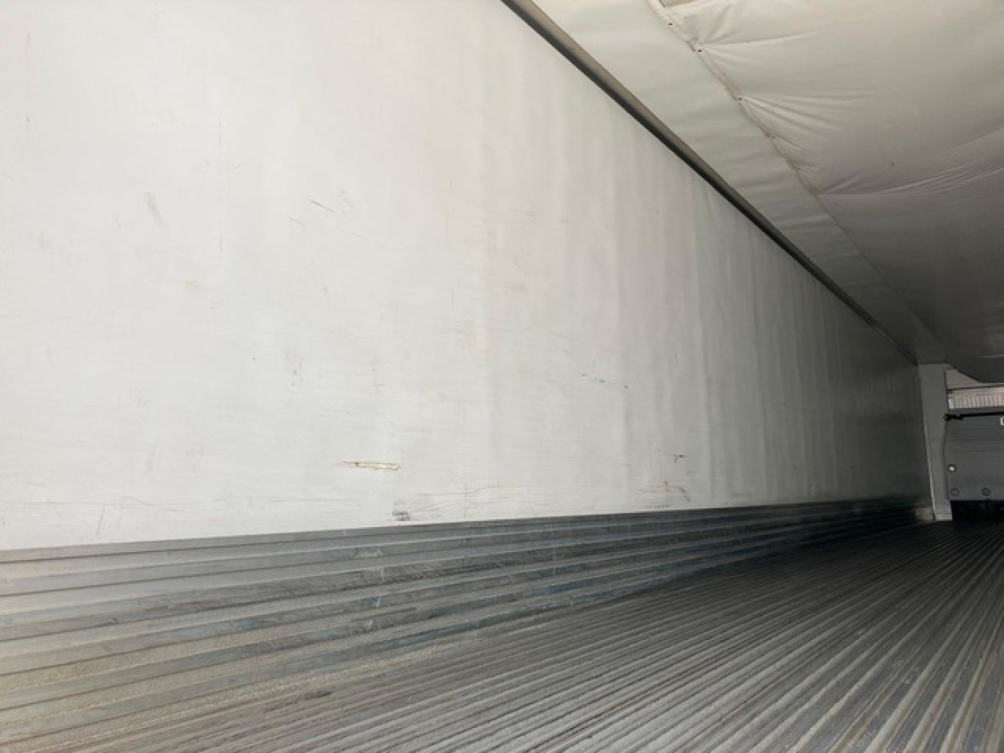 Refrigerated trailer interior showing ribbed metal floor and plain sidewall with a trailer door at rear.