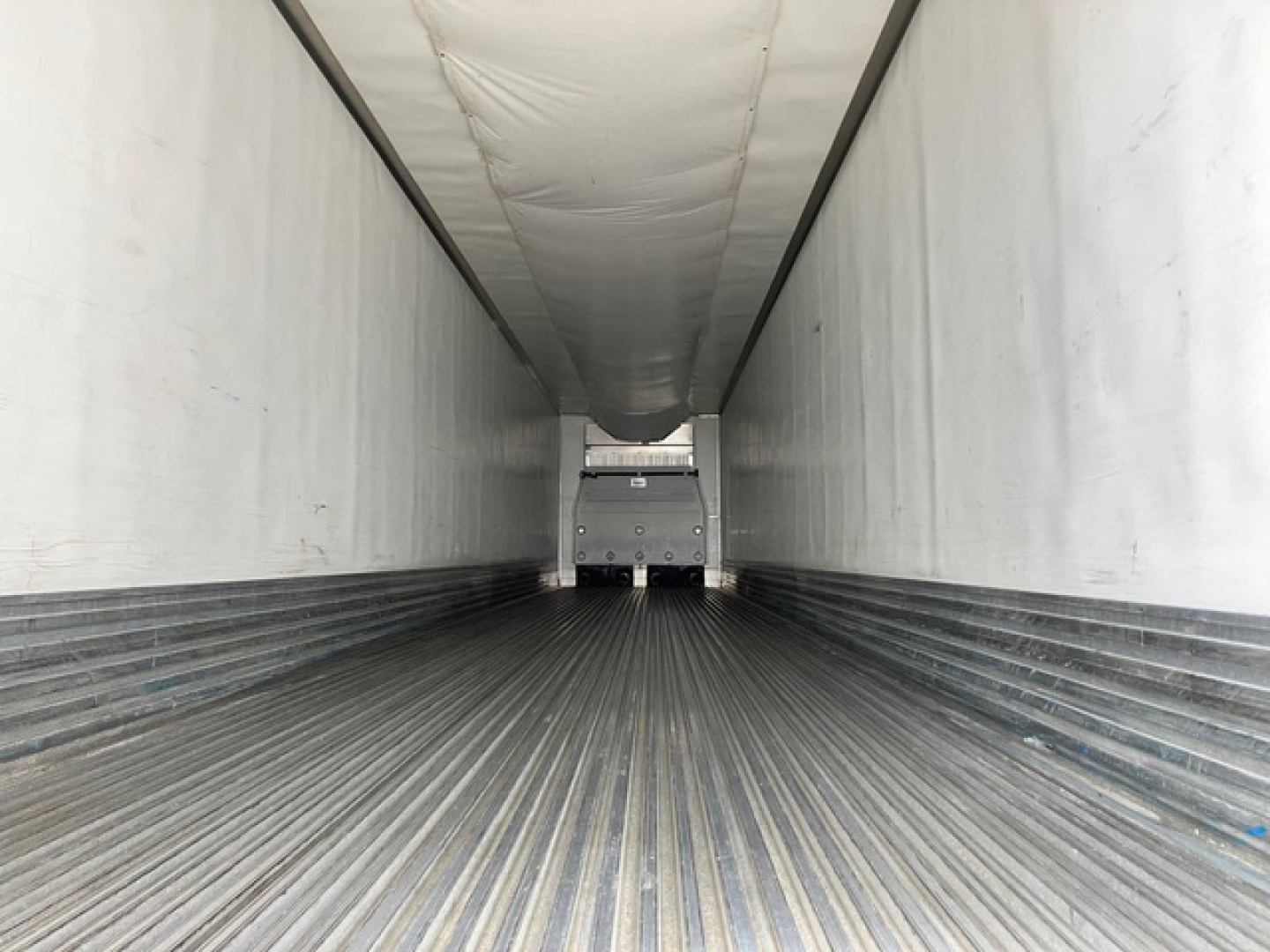 Trailer interior showing empty refrigerated trailer with corrugated metal floor and white insulated walls, rear doors closed.