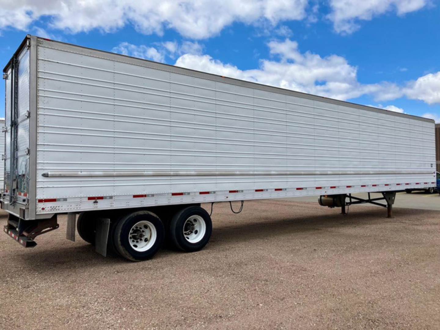 Long silver refrigerated trailer with dual rear axles and a raised nose. No visible branding on side. Clear blue sky.