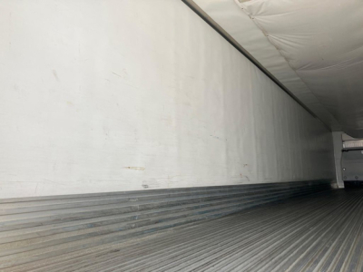 Refrigerated trailer interior showing ribbed metal floor and plain sidewall with a trailer door at rear.