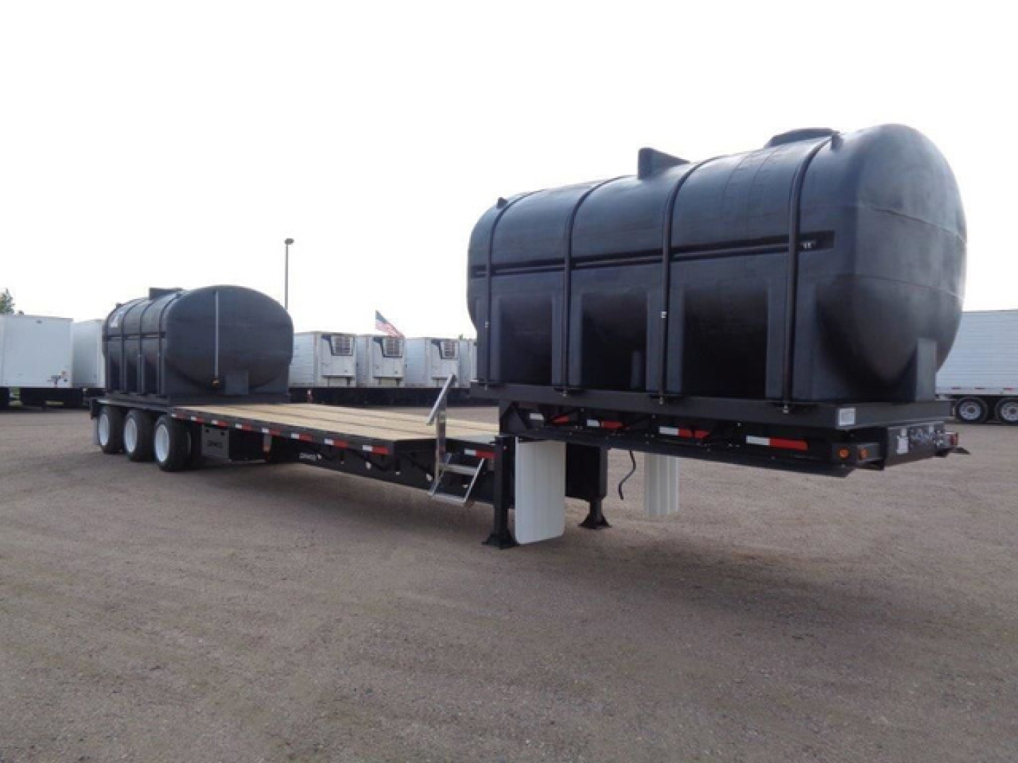 Demco Liquid Tender trailer showing two large black cylindrical tanks on a flatbed with triple-axle configuration and support jacks.