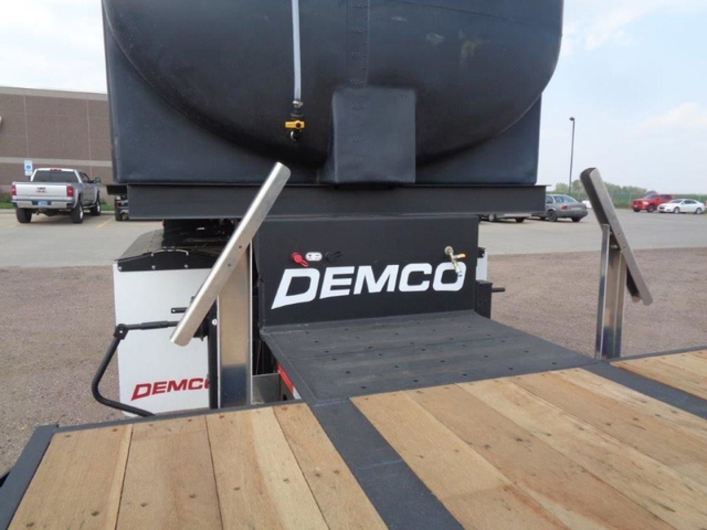 Demco liquid tender trailer with Demco branding visible on the rear, platform and storage box, showing a wooden deck and metal rails.