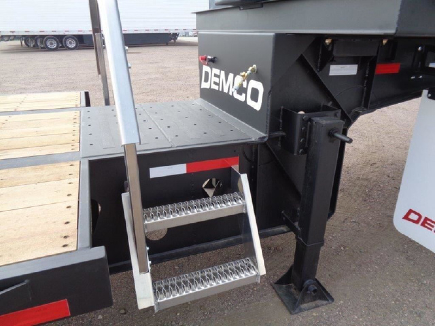 Demco Liquid Tender trailer rear step area with metal steps and black frame, brand name DEMCO visible on side, wooden deck to left and support legs in view.