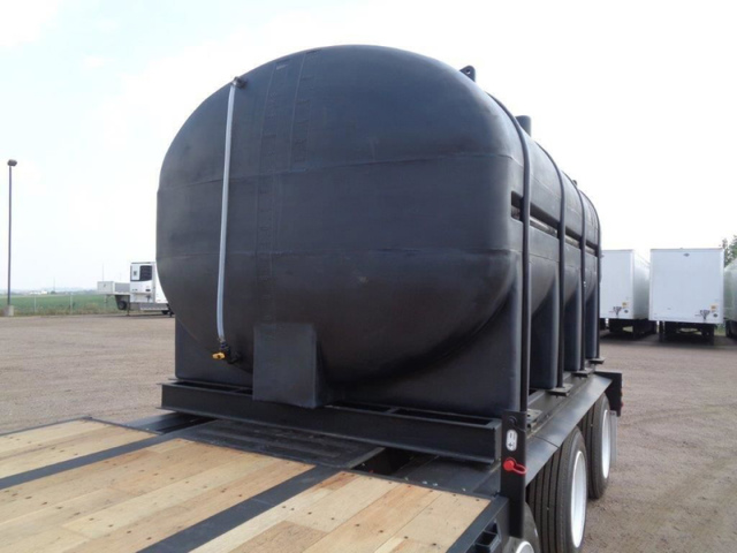 Demco liquid propane? wait no: image shows a large cylindrical black tank mounted on a dual-axle trailer with wooden deck, tubing strapped along the tank.