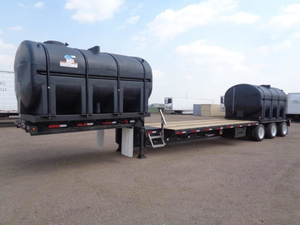 Trailer with two large black cylindrical tanks mounted on a flatbed trailer, Demco Liquid Tender branding visible, long dual-axle trailer in an outdoor lot.