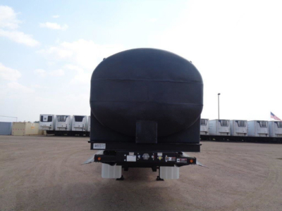 Demco Liquid Tender trailer nose showing rounded front tank and rear hitch area with support legs and wheels in a dealership lot.
