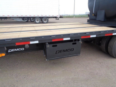 Trailer chassis showing Demco logo and a rectangular metal toolbox mounted under the flatbed.