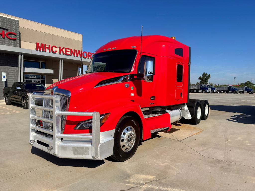 Kenworth T680 conventional sleeper truck in red, front left view, chrome bumper guard, dealership lot