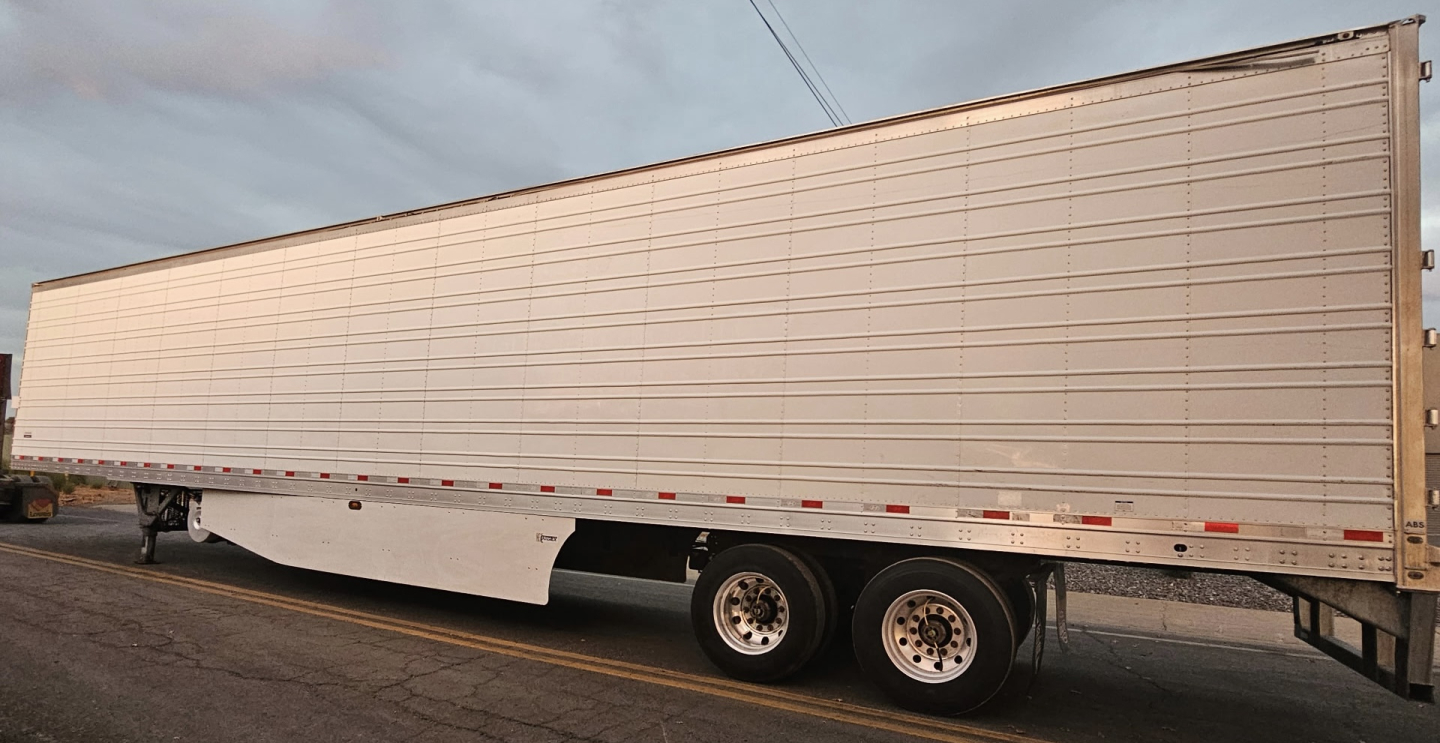 Trailer side view showing large rectangular aluminum reefer trailer with white reflective tape and dual rear axles.