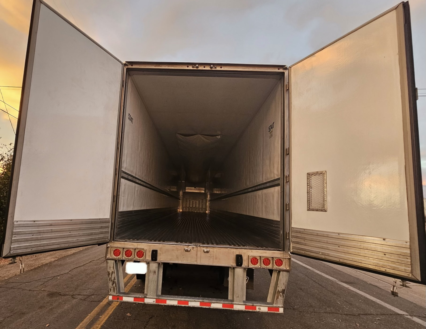 Trailer rear doors open showing empty refrigerated cargo area with metal floor and interior walls.