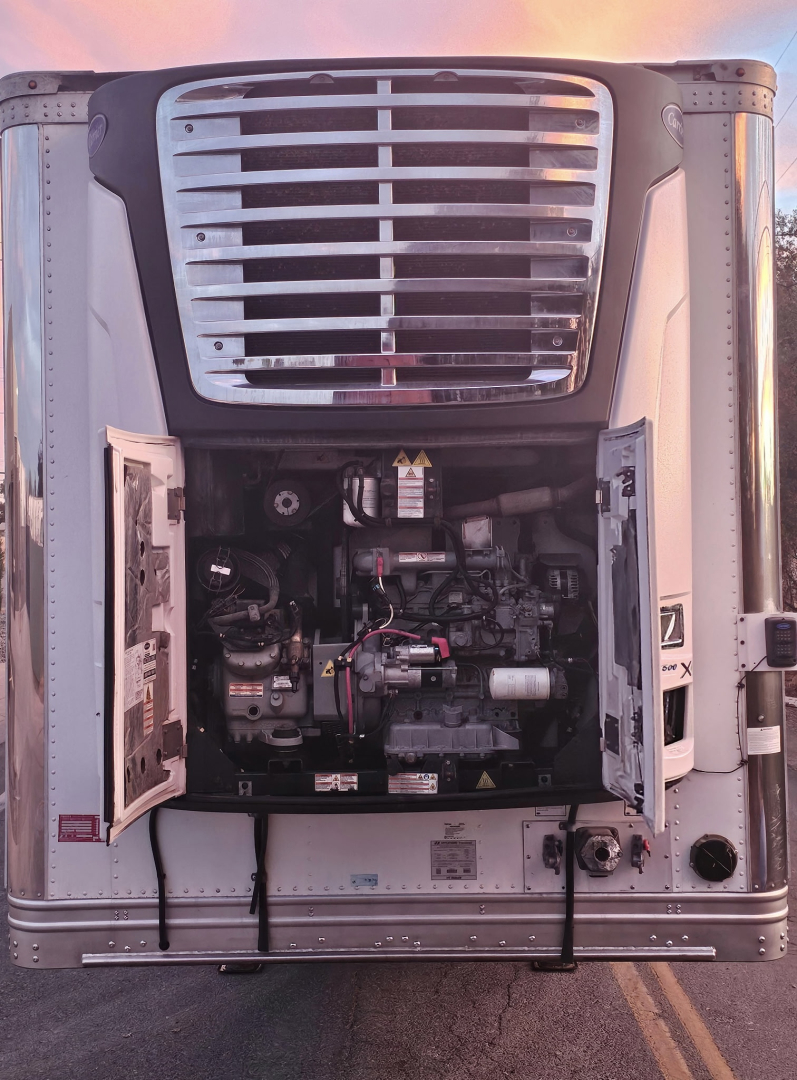 Truck refrigeration unit or engine bay of a reefer trailer with open access panels, showing components, hoses, and wiring inside the unit compartment.