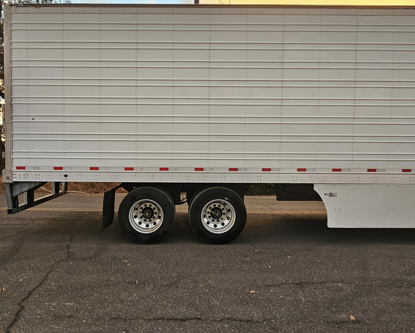Trailer side view showing dual rear axles and white refrigerated box, no visible text.