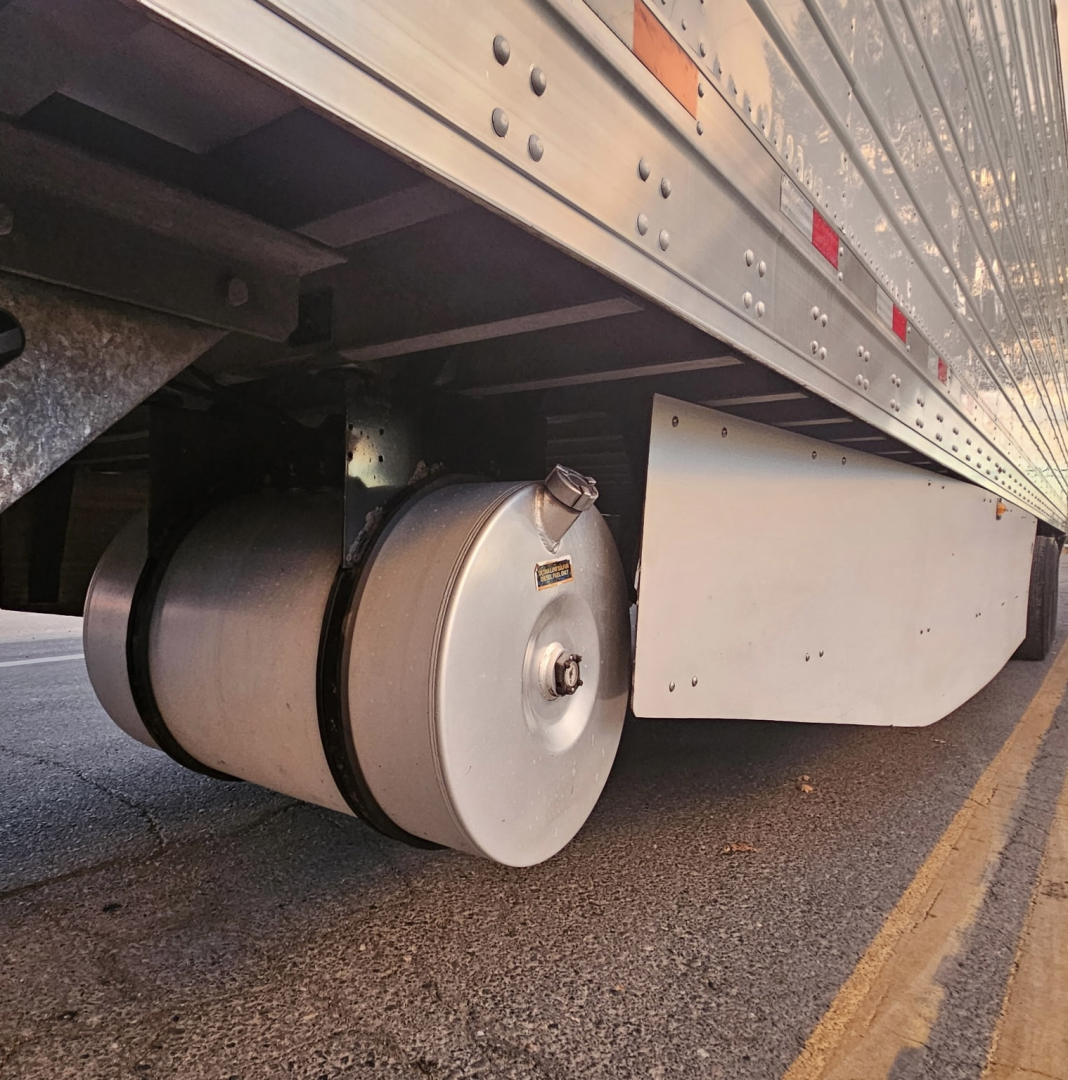 Trailer undercarriage showing dual cylindrical air springs/air bags and wheel area with metal frame and mudguard.
