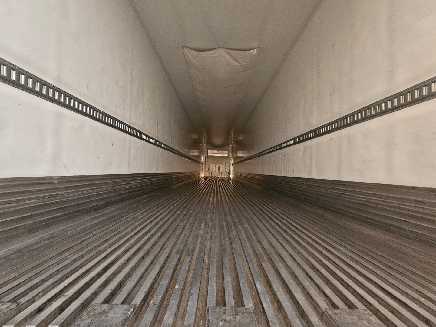 Trailer interior showing ribbed floor and sidewall tracks, empty cargo space, distant rear doors, no visible branding text.