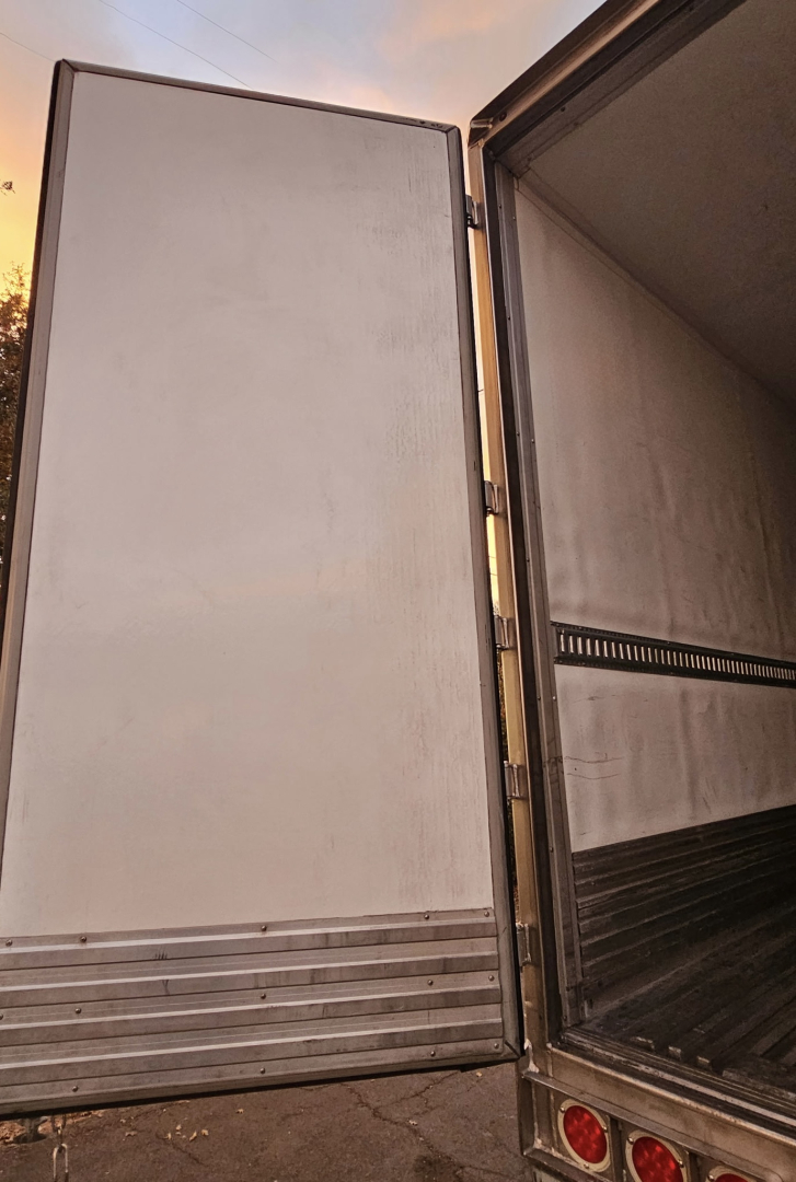 Trailer rear door open showing interior of refrigerated trailer with metal flooring and side wall rails.