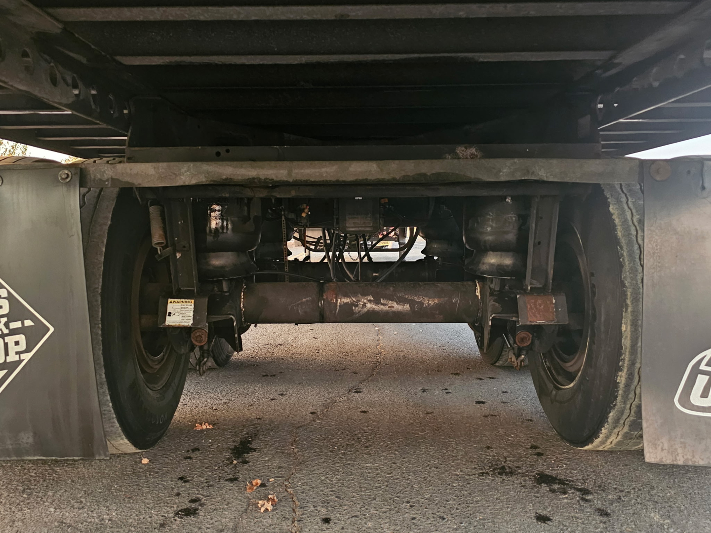 Trailer undercarriage showing axles, suspension, and dual wheels of a reefer trailer. Visible components include leaf springs, axles, and undercarriage frame.