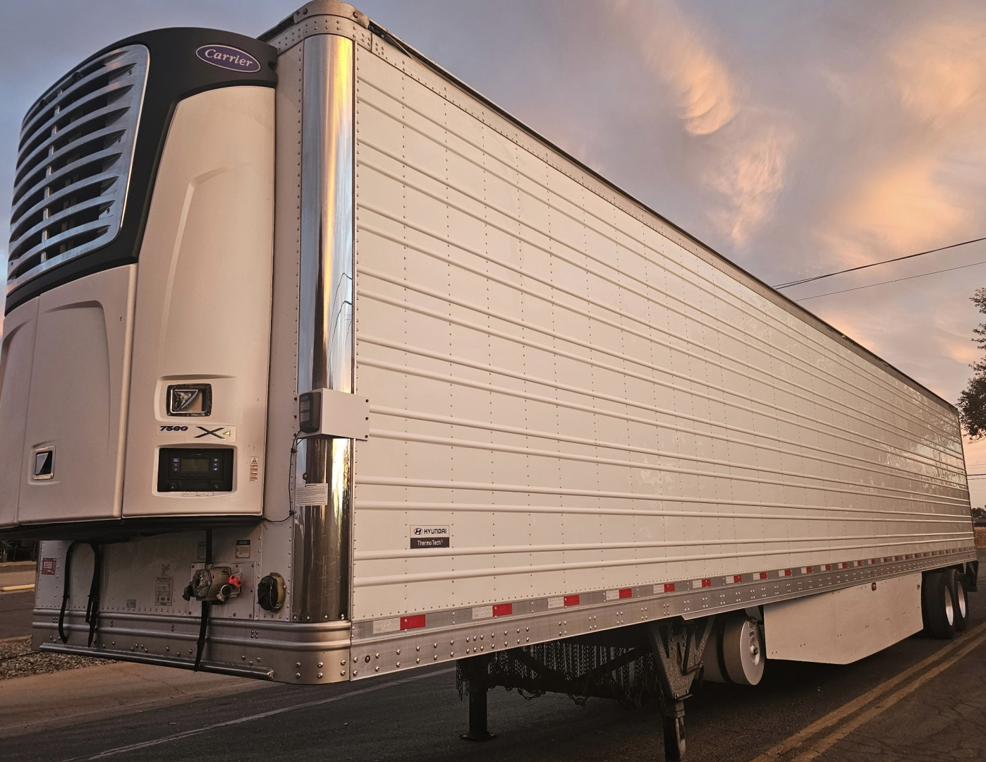 Trailer side view showing reefer trailer with Carrier refrigeration unit and silver aluminum panels.