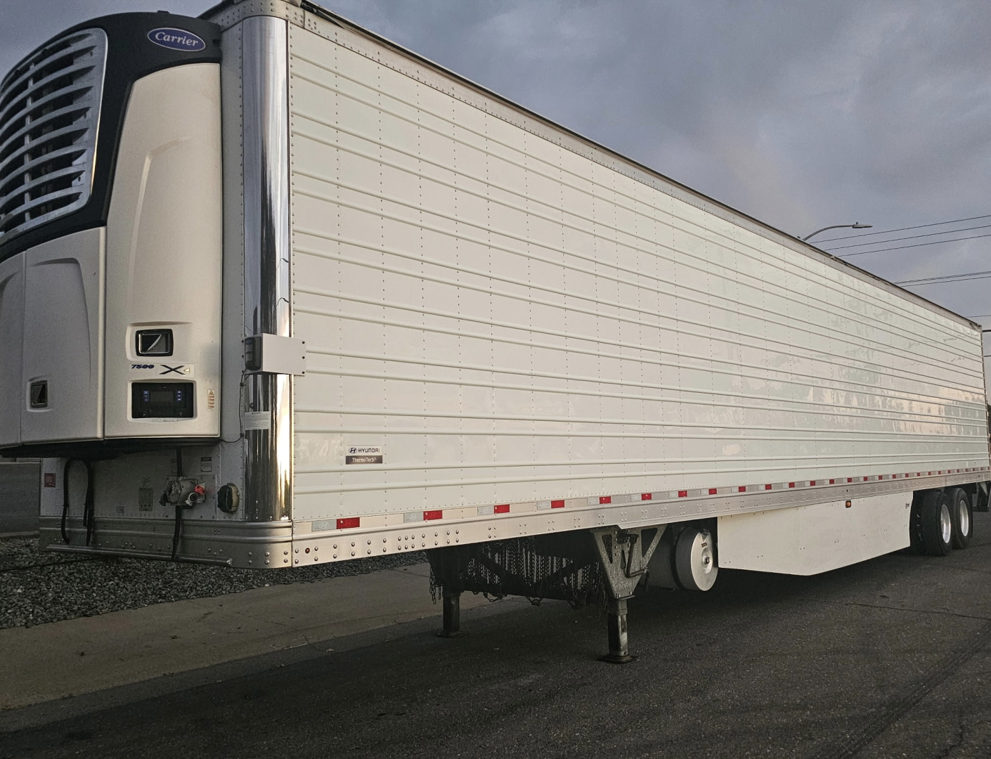 Trailer side view of a reefer trailer with ThermoTech TL branding, white curbside paneling and a Carrier refrigeration unit at the front left.