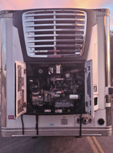 Truck refrigeration unit or engine bay of a reefer trailer with open access panels, showing components, hoses, and wiring inside the unit compartment.