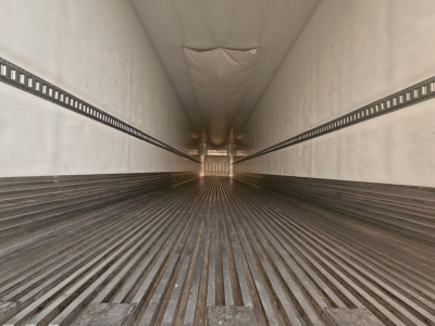 Trailer interior showing ribbed floor and sidewall tracks, empty cargo space, distant rear doors, no visible branding text.