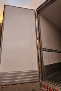Trailer rear door open showing interior of refrigerated trailer with metal flooring and side wall rails.