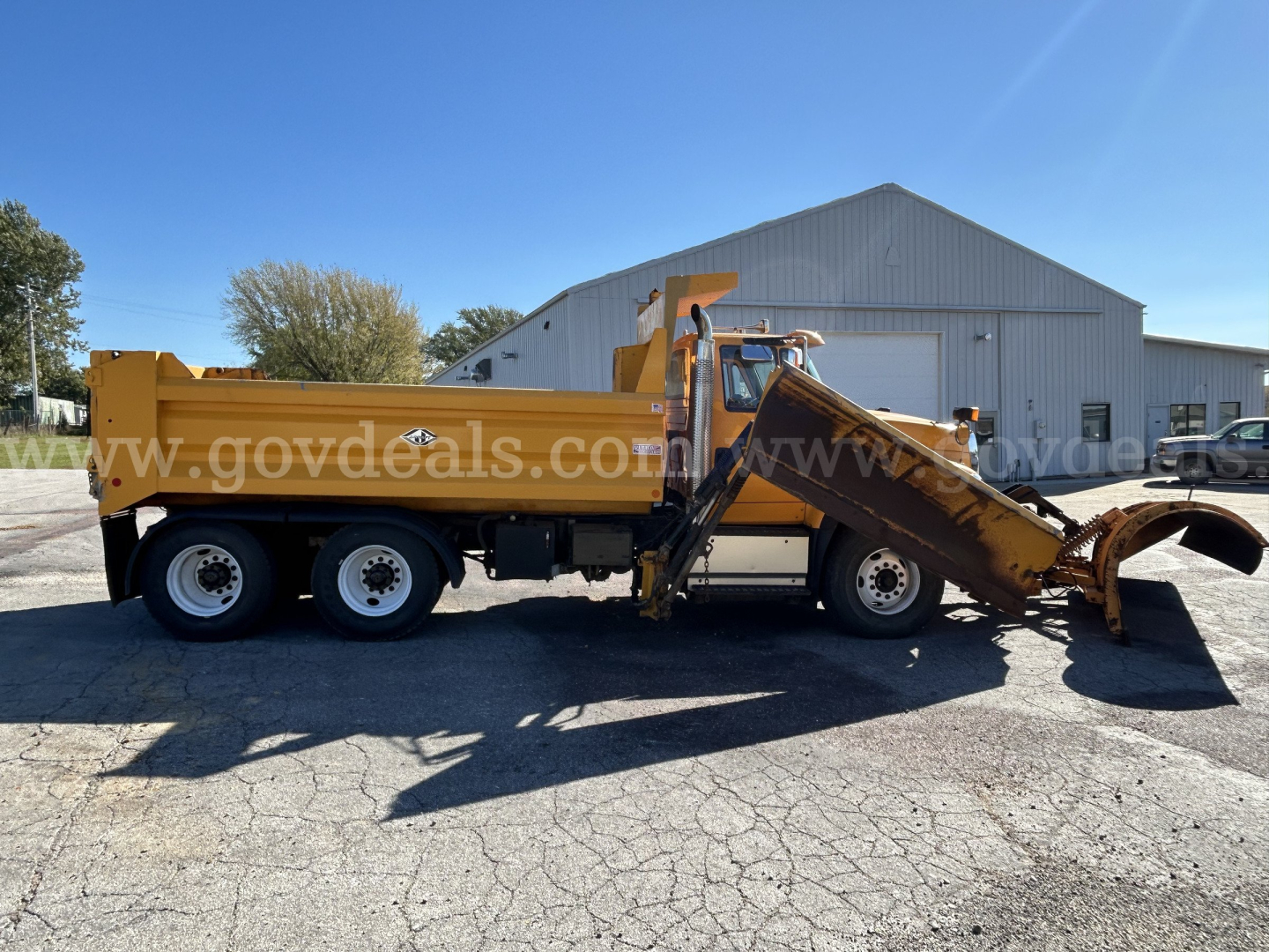 Side view of a 2016 International WorkStar 7600 plow truck in service, yellow dump bed, front cab with snow plow attachment, large metal blade at front-right, three axles.