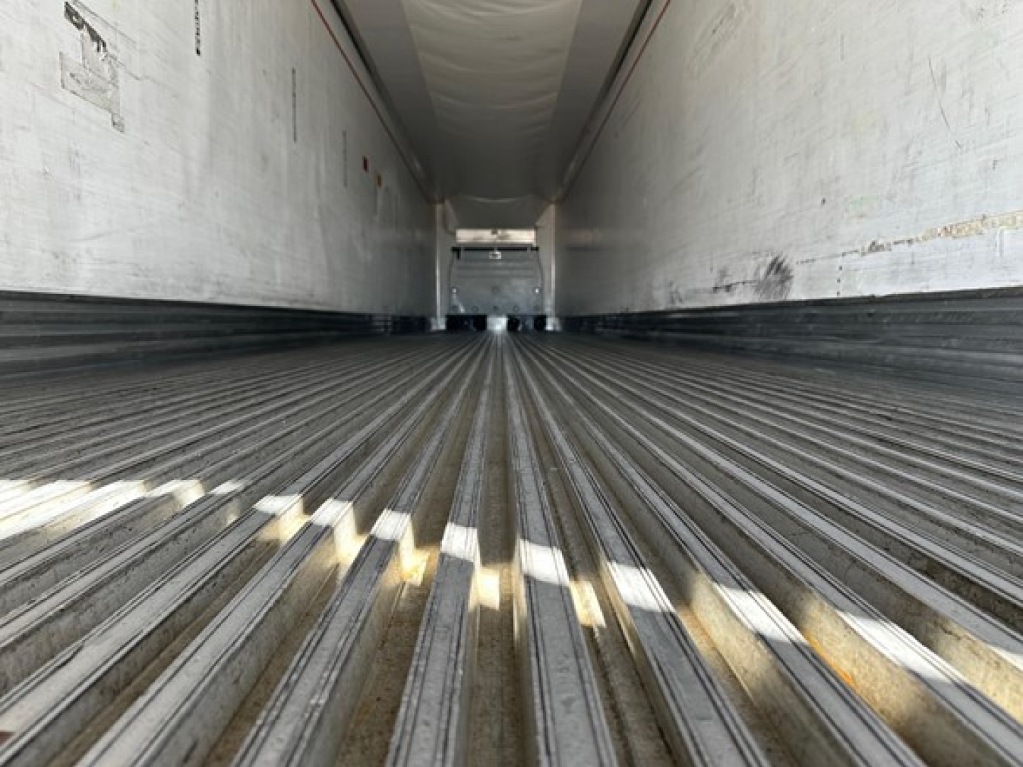 Trailer interior cargo area showing ribbed flooring and sidewalls, rear opening horizon visible in distance.