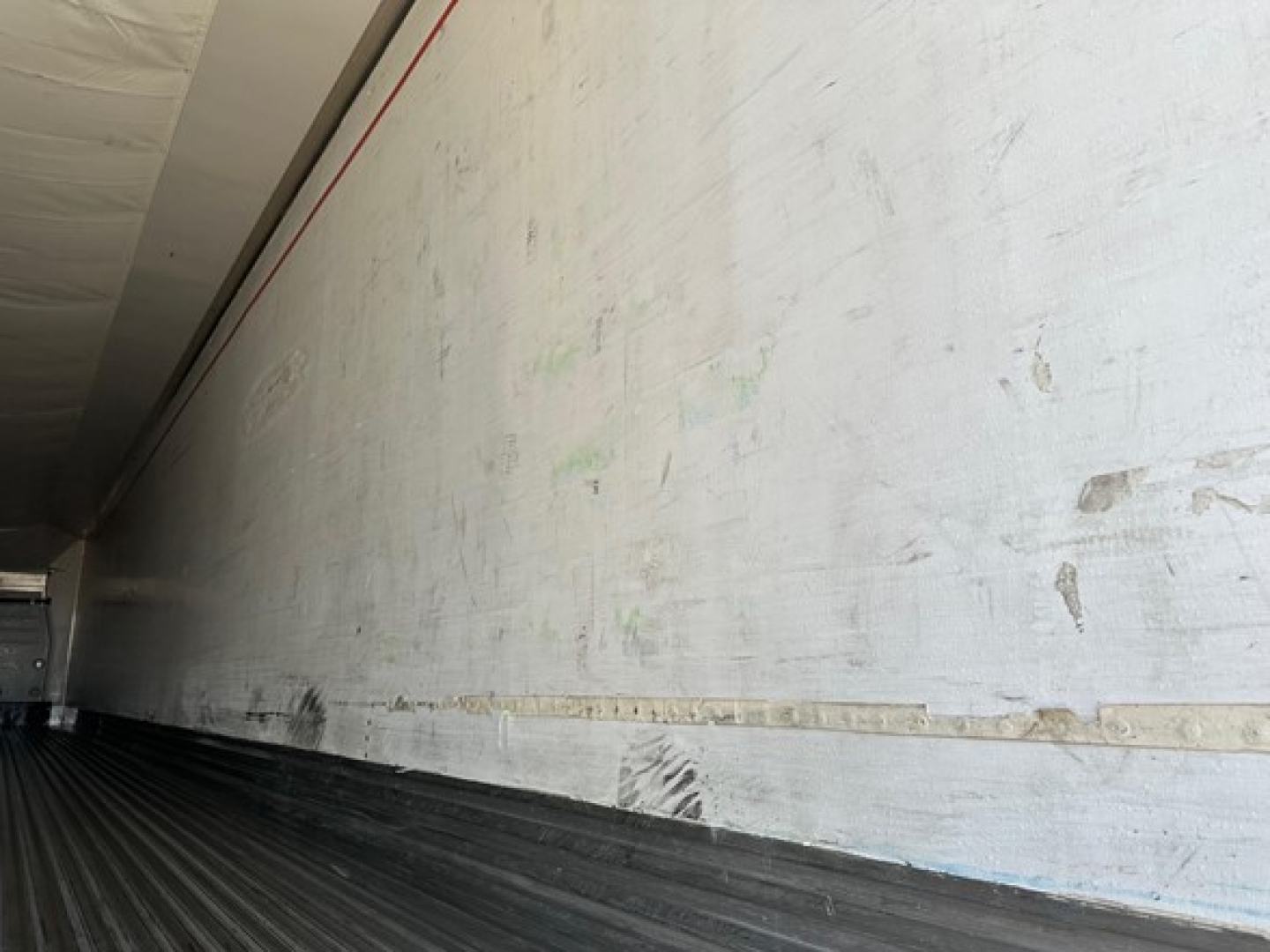 Trailer interior side wall with horizontal rail and faint marks inside a refrigerated trailer.