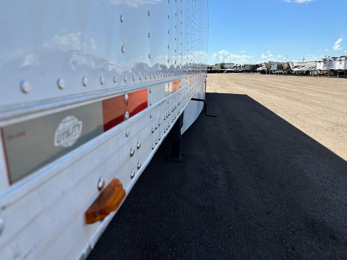 Trailer side of a 2017 Utility 3000R reefer trailer showing riveted aluminum wall with orange side marker, reflection on surface, and lot in background.