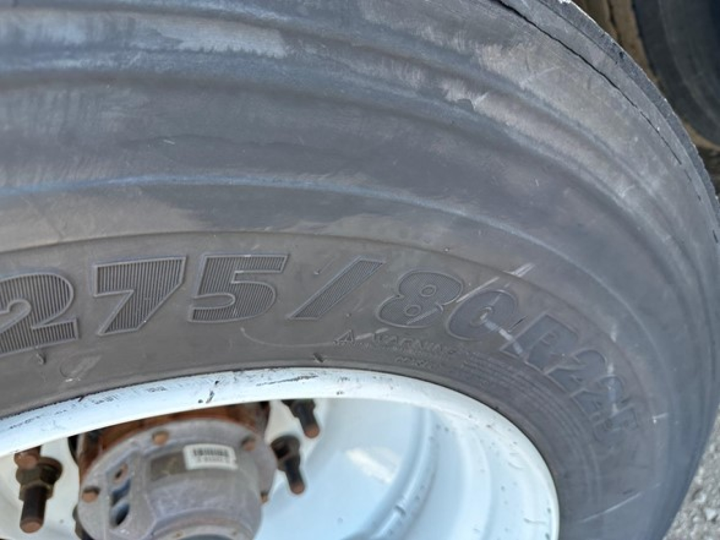 Trailer wheel and tire with visible tire size marking 275/80R; partial wheel hub showing rust around studs.