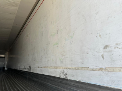 Trailer interior showing aluminum sidewall with wear marks and a wooden rail along the lower wall; ribbed floor visible.