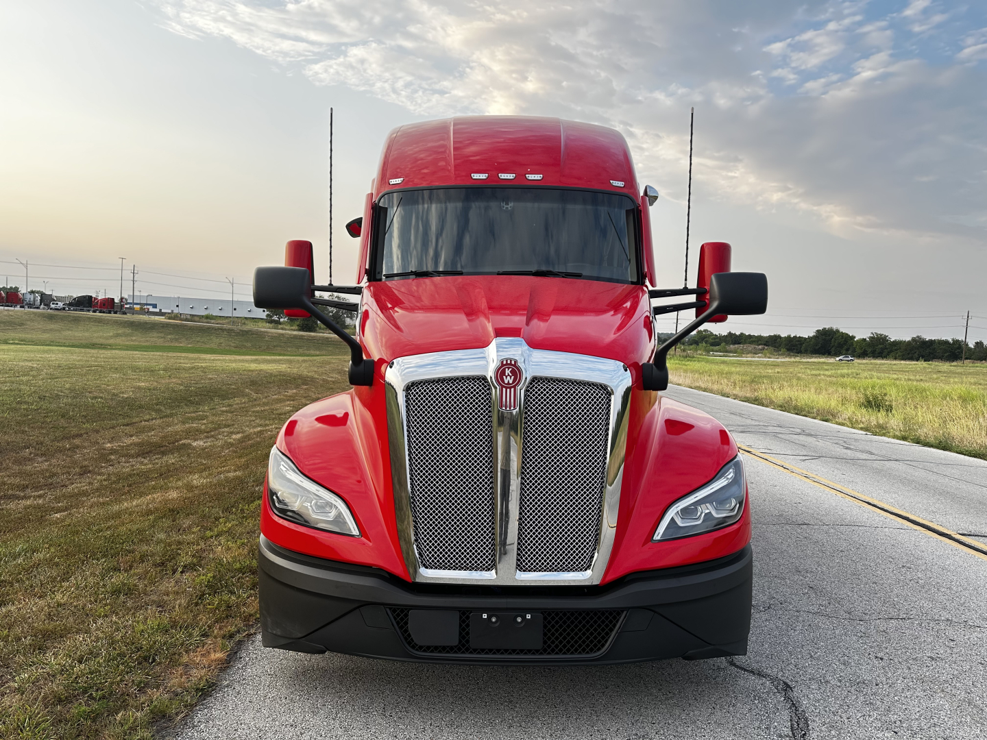 Kenworth T680 front view in red with large chrome grille, side mirrors, and sleeper cab, daytime outdoor setting.