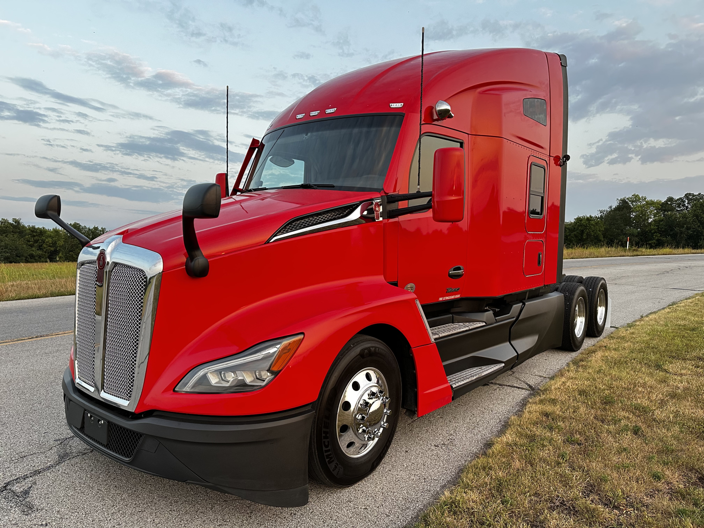 Kenworth T680 semi-truck side-angle view in red with sleeper cab, chrome grille, and black bumper.